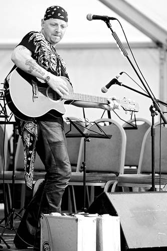 Black-and-white photograph of Wiggy performing with an acoustic guitar and microphone